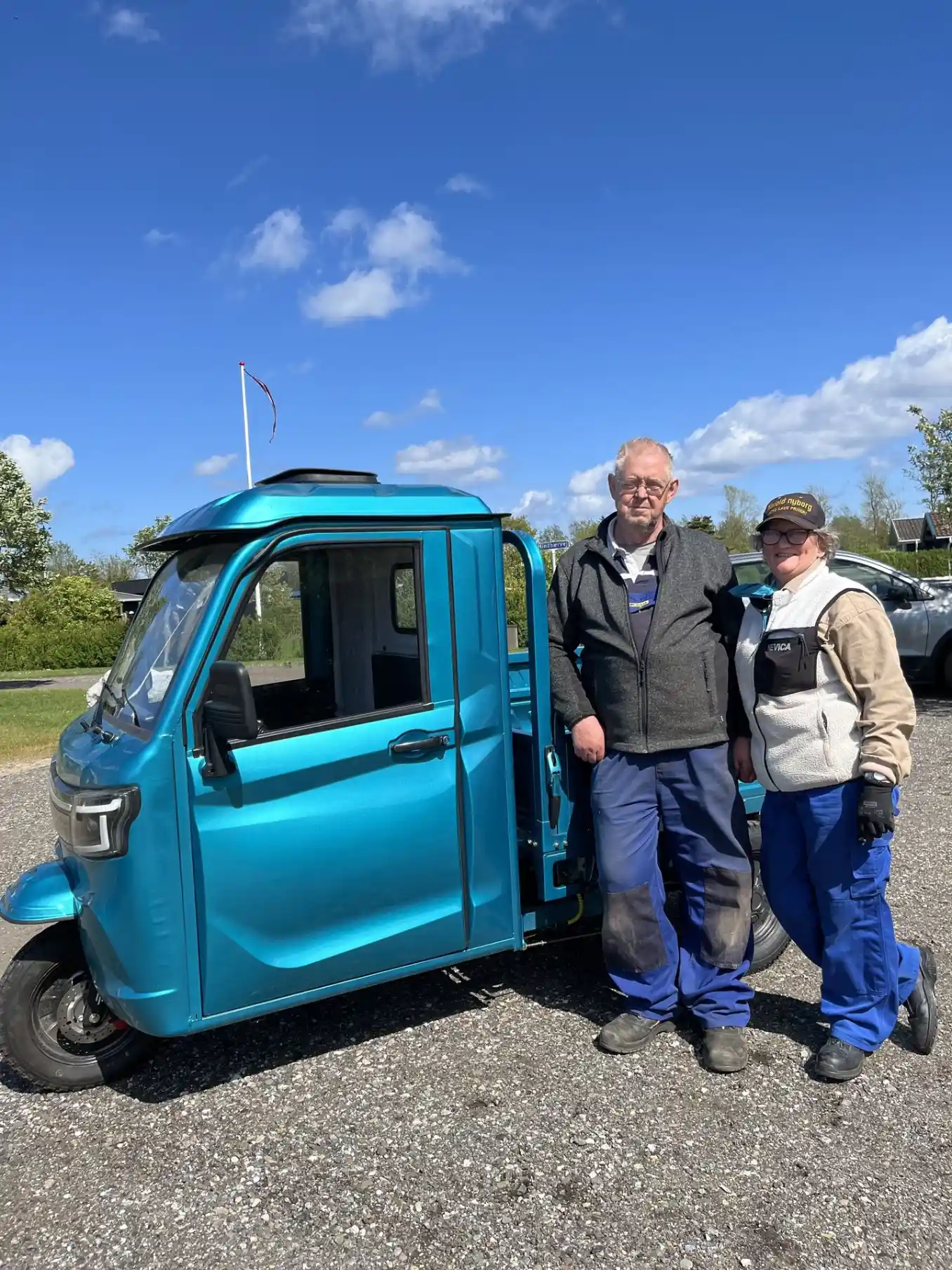 To glade kunder foran deres blå LuxCap kabinescooter i indkørslen