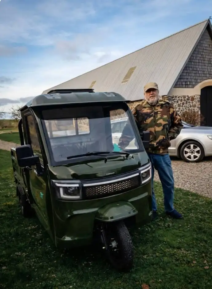 Grøn elektrisk kabinescooter testet af glad kunde på græsplæne